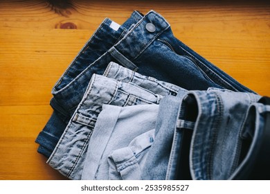 Beautiful stack of folded jeans in different shades of blue. Denim background. Jeans texture on wooden background - Powered by Shutterstock