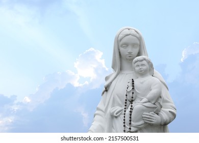 Beautiful Statue Of Virgin Mary And Baby Jesus With Rosary Beads Outdoors. Space For Text