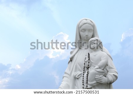 Beautiful statue of Virgin Mary and baby Jesus with rosary beads outdoors. Space for text