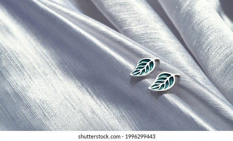 Beautiful sterling silver stud earrings in form of leaves lying on gray silk background. Jewelry fashion photography - Shutterstock ID 1996299443