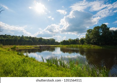 Beautiful still lake with trees on the horizon and white puffy clouds in the sky. Peaceful summer day at the cottage. Large green trees on a lake - Powered by Shutterstock