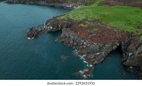 Beautiful stone cliff and green ocean water with small ripples. Clip. Aerial view of rocky coast.