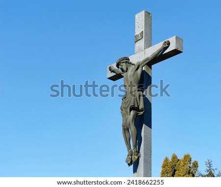 Beautiful stone sculpture of Jesus on the cross with a clear blue sky in the background placed in the city cemetery of Zapresic, Croatia