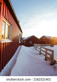 Beautiful Street Of Lofoten Village Covered By Snow Beyond Red Rorbuers At Sunset In Lofoten, Norway. Solitude Street With No Person And Blue Sky At Winter Season In The Artic Circle