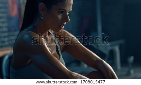 Beautiful Strong Fit Brunette in Sport Top and Shorts in a Loft Industrial Gym with Motivational Posters. She's Catching Her Breath after Intense Fitness Training Workout. Sweat All Over Her Face.