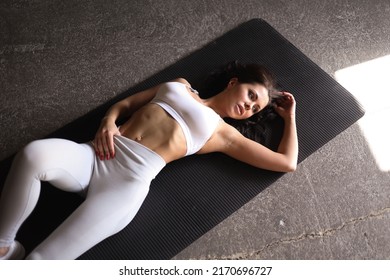 beautiful strong muscular woman doing stretching in gym. Healthy middle-aged adult woman in   sportswear stretch alone. Fit thin girl doing sports indoors, training hard on black mat