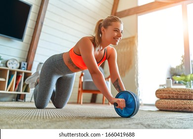 Beautiful strong woman in sportswear is working out with exercise wheel at home in the living room. Sport and recreation concept. - Shutterstock ID 1660419688