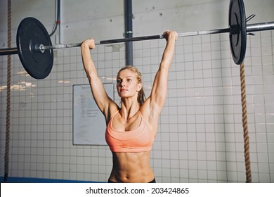 Beautiful Strong Young Woman With Barbell And Weight Plates Overhead. Fit Young Female Athlete Lifting Heavy Weights. Caucasian Female Model Performing Crossfit Exercise.