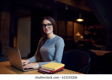 Beautiful Student Of Design Faculty Thinking About New Ideas For Creative Project While Typing Text Message On Keyboard Of Modern Laptop Using 4G Wireless Internet Connection Sitting In Coffee Shop