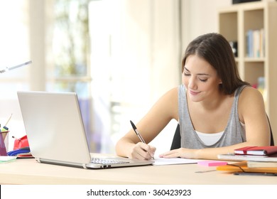 Beautiful student studying on line and learning writing notes in a desk at home