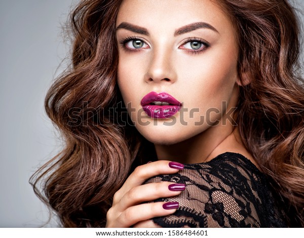 Beautiful and stunning woman with bright purple\
lipstick on lips and fingernails.  Young caucasian gorgeous adult\
girl with long brown hair. Model. Closeup woman\'s portrait. Vivid\
make-up. Sexy female