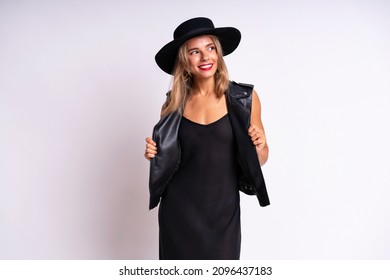 Beautiful Stunning Woman With Red Full Lips, Elegant Casual Black Dress, Hat And Leather Vest Posing On White Background. Free Spirit, Rock N Roll Style, Having Fun.