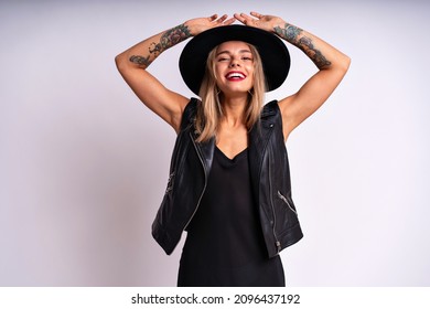 Beautiful Stunning Woman With Red Full Lips, Elegant Casual Black Dress, Hat And Leather Vest Posing On White Background. Free Spirit, Rock N Roll Style, Having Fun.