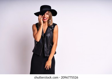 Beautiful Stunning Woman With Red Full Lips, Elegant Casual Black Dress, Hat And Leather Vest Posing On White Background. Free Spirit, Rock N Roll Style, Having Fun.