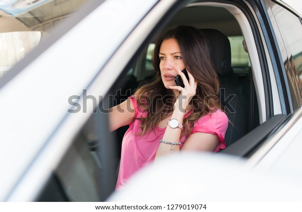 Beautiful stunning woman sitting in\
the car and talking on the phone and driving. Woman buying a new\
car. Angry woman because bank loan and credit is\
cancelled.