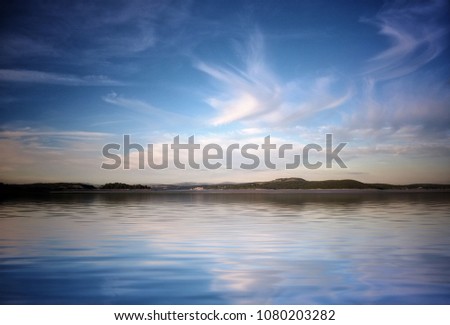 Beautiful stylised image of sky and fluffy evening clouds reflected in calm sunset blue water with distant hills taken in morecambe bay England