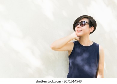 A Beautiful Stylish Asian Woman Wearing 100% UV Light Eyes Protection Sunglasses Standing Next To The White Wall With Beautiful Leaves Shadow. Sunscreen, SPF, Facial Skincare, Outdoor, Copy Space