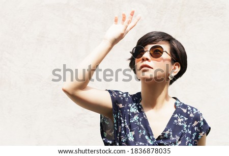 Beautiful & Stylish Asian woman wearing 100% UV light eyes protection sunglasses, stand and raise her hand to block out bright glare and sunlight to avoid ultraviolet rays. UV exposure, Aging, Optical