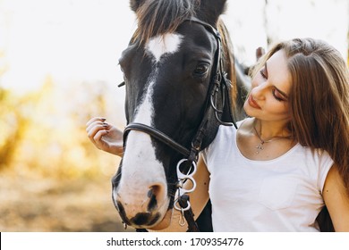 Beautiful stylish blonde woman near horse on ranch. Smiling girl hugging a horse. Human and animals relationship concept