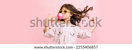 Beautiful, stylish, cute little girl with wavy hair posing in sunglasses with bubblegum over pink background. Childhood, fun, style. Concept of emotions, facial expression, sales, ad, fashion