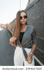 Beautiful stylish elegant glamorous girl with vintage sunglasses in fashion casual clothes with a shirt stands near a black brick wall on the street - Shutterstock ID 2394617605