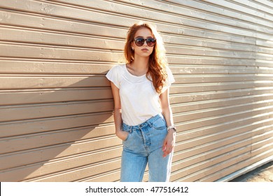 Beautiful stylish girl in a vintage blue jeans and white T-shirt standing near a wooden wall.