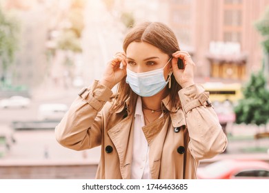 Beautiful stylish girl wear medical face mask on sunny city street. Young elegant happy hipster woman put on protective face mask outdoors. Urban fashion outfit, lifestyle. COVID-19 quarantine, travel