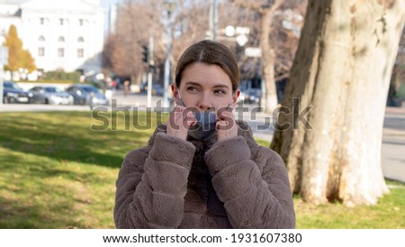 Beautiful stylish girl wear medical face mask on sunny city street. Young elegant happy hipster woman put on protective face mask outdoors. Urban fashion outfit, lifestyle. COVID-19 quarantine, travel