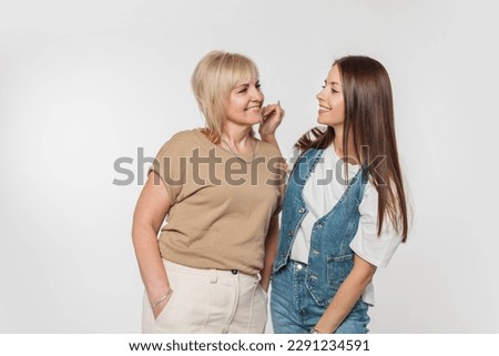 Beautiful stylish happy woman daughter with smile and elderly mother in fashionable casual clothes have fun on a white background in the studio