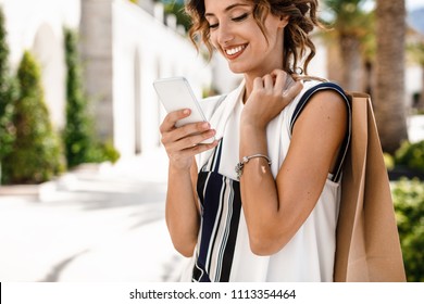 Beautiful Stylish Smiling Caucasian Woman Looking At Her Cell Phone And Holding Shopping Bag.