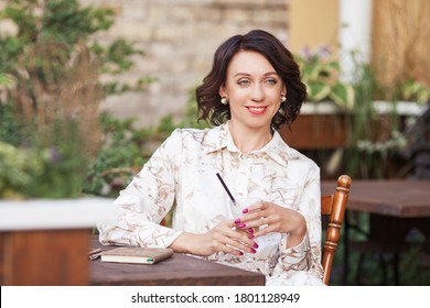 Beautiful Stylish Woman In Beige Dress Drinking Coffee Outdoors At The Cafe. Portrait Of Happy Female In Open Air Cafe Not  Looking At Camera 