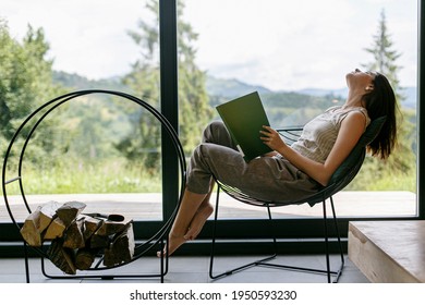 Beautiful stylish woman relaxing with book in modern chalet with amazing view on mountain hills. Leisure time. Young female in casual clothes reading book on chair at firewood. - Shutterstock ID 1950593230