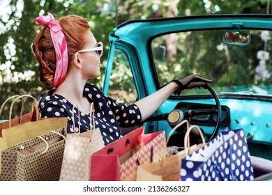 Beautiful Stylish Woman In Vintage Bright Dotted Clothes And Glasses Is Driving Mint Old Car After Shopping. Fashion Pin-up Girl Bought Goods And Products. Retro Style Concept. Black Friday Sale.