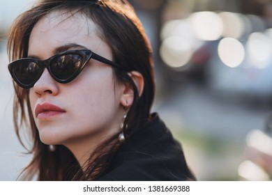 Beautiful stylish young girl model at cateye sunglasses walks around the city and poses