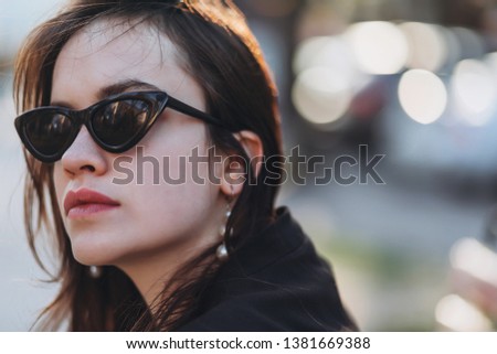 Beautiful stylish young girl model at cateye sunglasses walks around the city and poses
