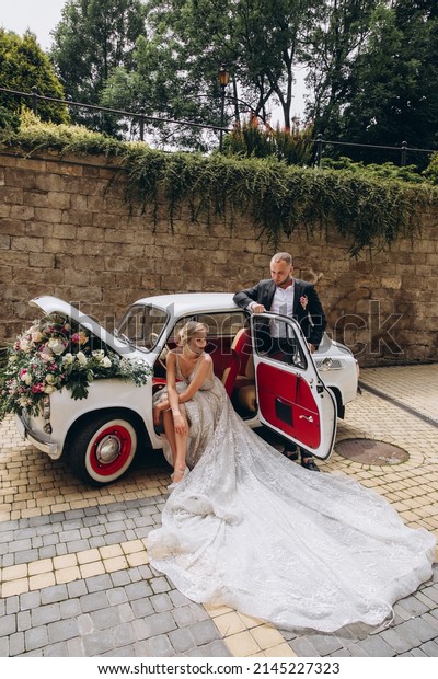 Beautiful stylish young successful kissing couple\
enjoying near the retro car with flowers at wedding walk in the\
tropical country or\
island