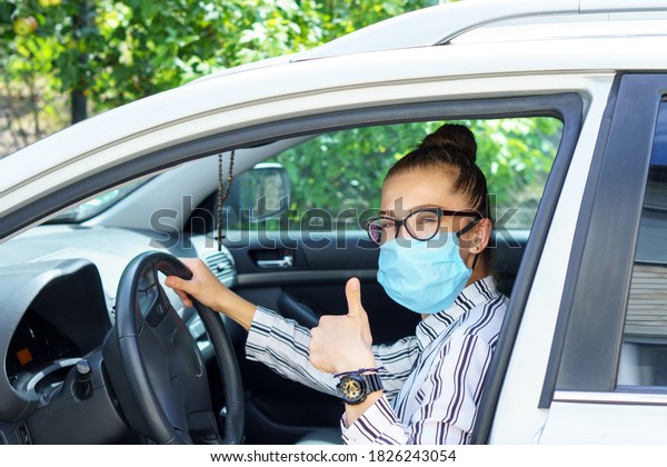 beautiful successful smiling rich business woman in\
medical protective mask sitting in gray car, wearing glasses\
showing thumbs up super, prosperous business lady style Lady is\
driving a car for\
work