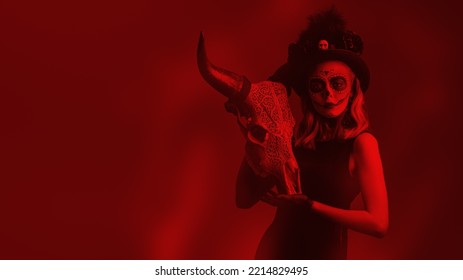 Beautiful Sugar Skull Girl Holds A Cow Animal Skull With Ethnic Ornaments On A Red Background With Copy Space. The Traditional Look Of Calavera Catrina. Day Of The Dead. Dia De Los Muertos. Halloween.