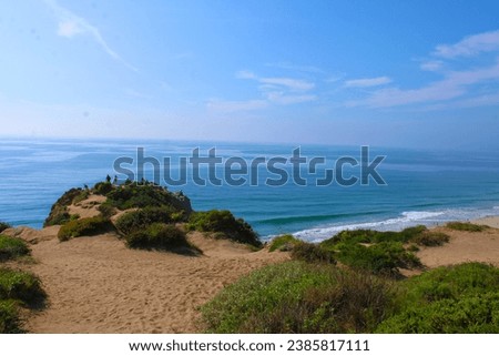 a beautiful summer landscape at Point Dume State Beach with vast blue ocean water and waves rolling into the beach, rocks along the cliffs and blue sky in Malibu California USA
