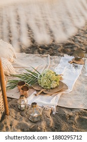 Beautiful summer picnic on the beach at sunset in boho style. Straw basket with flowers on linen blanket on the sand. Vegetarian eco idea for weekend picnic.