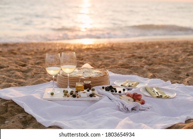 Beautiful summer picnic at sunset on beach with white wine, pizza, cheese, olives and fresh fruits.