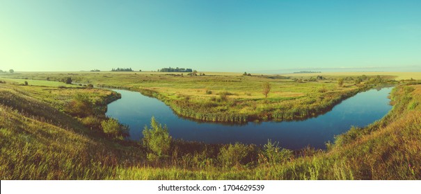 Beautiful summer rural nature landscape. Sunny panoramic view of blue river and green meadows with trees on background.Retro and vintage colors. Summer background. Beauty of summer nature.