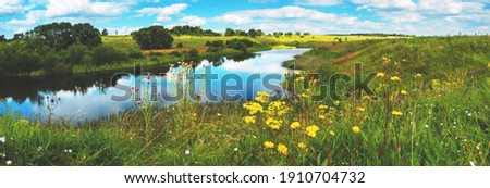 Beautiful summer or spring panoramic rural landscape with calm river and green hills with blooming wild flowers and trees at sunny summer day.River Upa in Tula region,Russia.