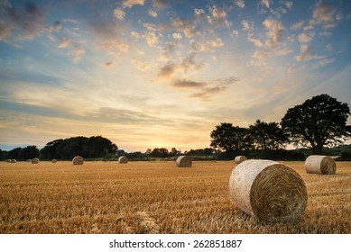 Beautiful Summer sunset over field of hay bales in countryside landscape