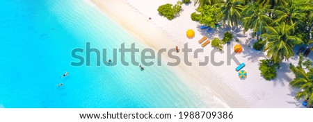 Beautiful summer tropical beach with white sand, palm trees, turquoise ocean water and tourists swimming in clear transparent  turquoise water. Panoramic aerial view. Ultra-wide background image.