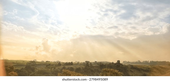 Beautiful sun rays breaking through morning clouds over a scenic green hill and rural landscape.
