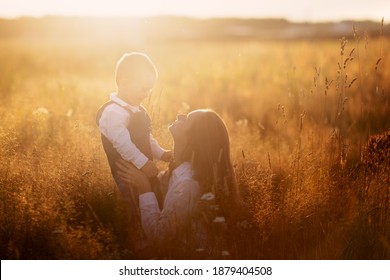 Beautiful sunny photo of motherhood, Caucasian mom with long hair in summer at sunset in the grass with her son toddler. Back light, soft focus and toning