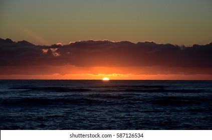 Beautiful sunrise cloudscape over ocean background. Sun rays beaming through picturesque clouds above sea. Blue sky with clouds, sea and sun on the horizon. Beautiful sunrise over the quiet calm sea.