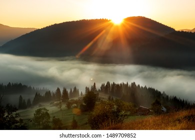 Beautiful Sunrise In The Mountains. Small Houses In A Meadow Among A Cone Of Coniferous Trees In The Fog. Great Awakening.
