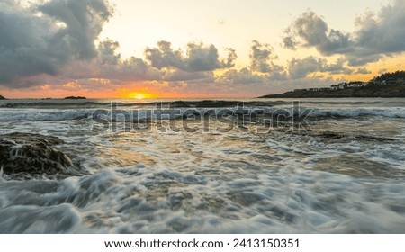 Beautiful sunrise on the beach. Seascape during morning golden hour. The sea water is wavy and the sky is cloudy.